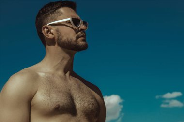 Kum ve mavi gökyüzü bulutlu üzerinde beyaz sunglesses kot ve beyaz tişört giyen güçlü ticari yüz erkek modeli 