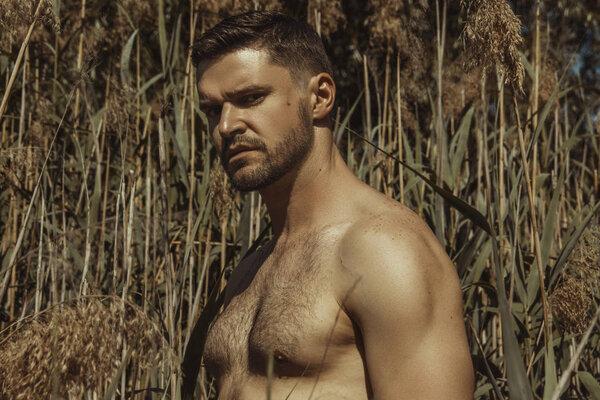 Sexy strong bearded male hunk in red swim shorts on the water background with summer vibes