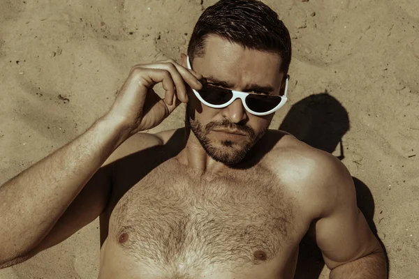 Strong commercial face male model  wearing white sunglesses jeans and white t-shirt  on sand and  blue sky with clouds