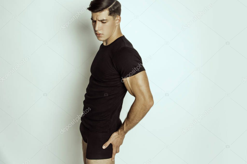 Muscle strong beautiful stripped male model in black t-shirt and black underwear on grey isolated font background