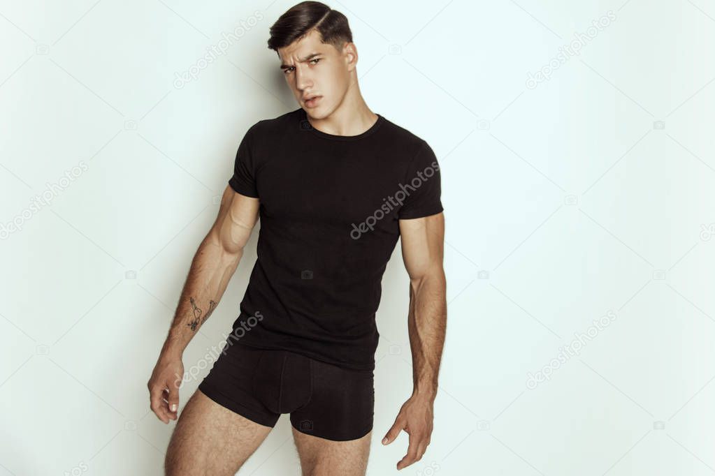 Muscle strong beautiful stripped male model in black t-shirt and black underwear on grey isolated font background