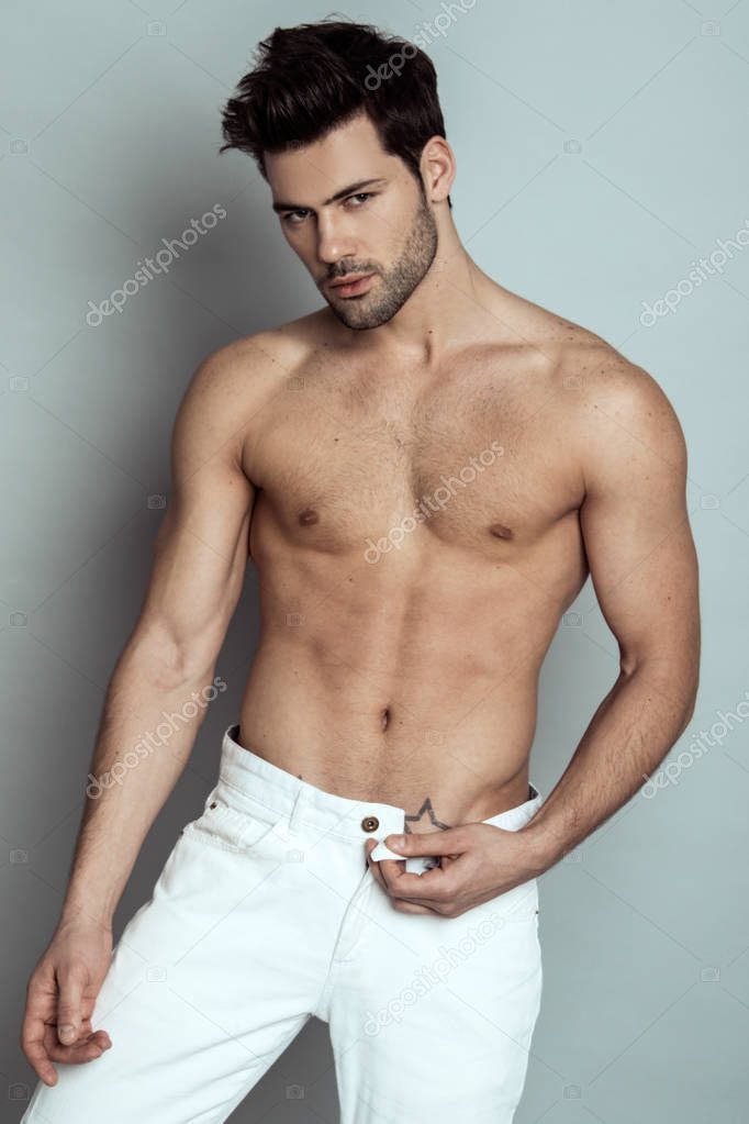 Muscle strong beautiful stripped male model in denim jeans with white t-shirt on grey isolated font background