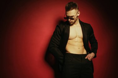 Kas gücü yüzlü, güzel, soyulmuş, sıradan görünümlü, kot pantolon ve takım elbiseli, yeşil gözlüklü, bej renkli, izole font arka planda sarı ışık takan erkek model.