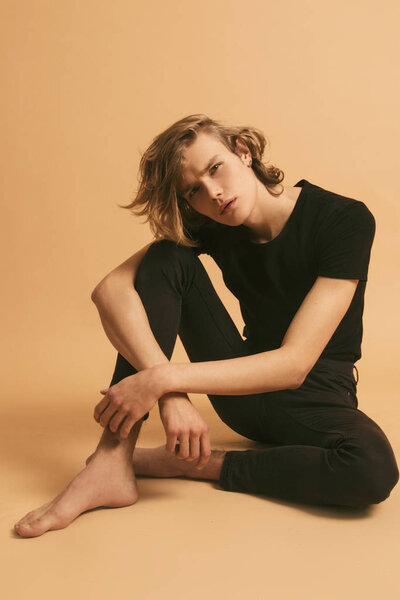 Muscle blonde beautiful stripped male model with long hair in casual look on beige brown isolated font background