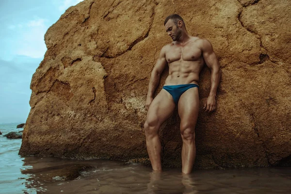 Strong face muscle male model on the nature background with sand stones and water on the beach on the sunset