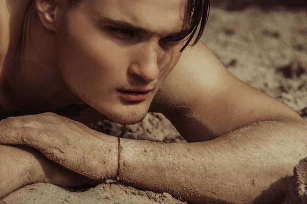 Strong face male model on the nature background with sand and water and sky on the beach on the sunset