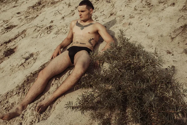 Strong face male model on the nature background with sand and water and sky on the beach on the sunset