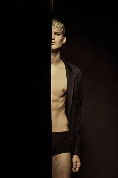Handsome stripped blonde male model wearing black suit on black isolated font background
