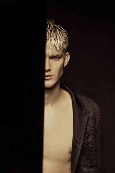 Handsome stripped blonde male model wearing black suit on black isolated font background