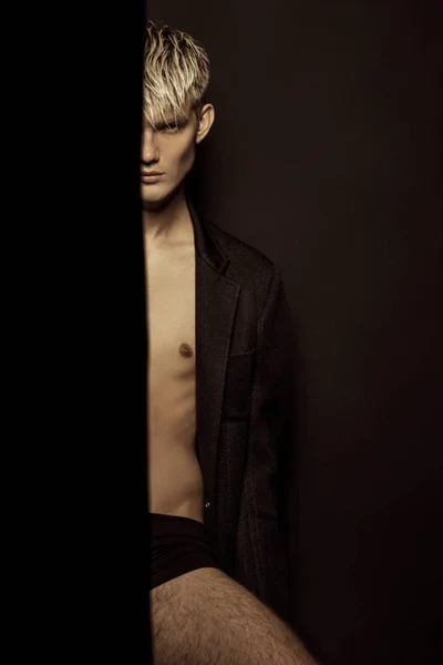 Handsome stripped blonde male model wearing black suit on black isolated font background