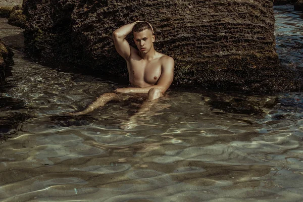 Strong face male model on the nature background with rocks and water on the beach on the sunset