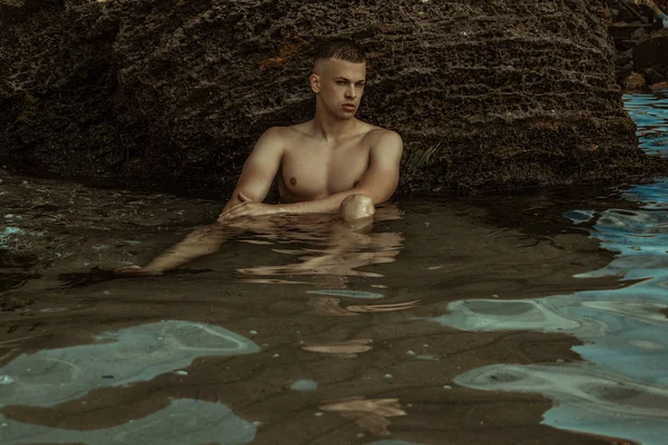 Strong face male model on the nature background with rocks and water on the beach on the sunset