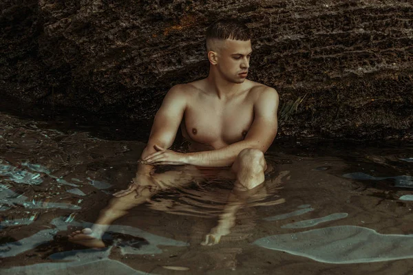 Strong face male model on the nature background with rocks and water on the beach on the sunset