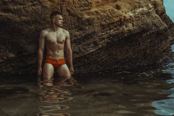 夕日のビーチで岩や水と自然の背景に強い顔男性モデル — ストック写真