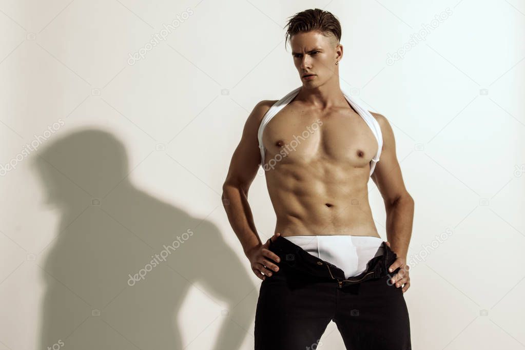 Muscle strong beautiful stripped male model in denim black jeans on white isolated font background