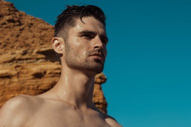 Gün batımında sahilde kayalar kum ve su ile doğa arka planda güçlü yüz erkek modeli