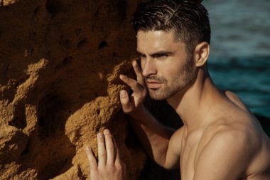 Gün batımında sahilde kayalar kum ve su ile doğa arka planda güçlü yüz erkek modeli