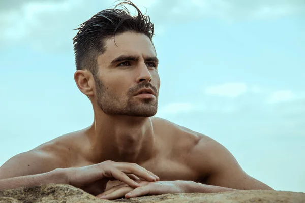 Strong face male model on the nature background with rocks sand and water on the beach on the sunset