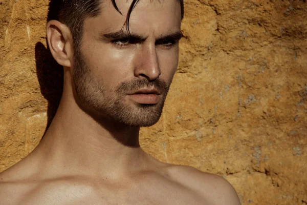 Strong face male model on the nature background with rocks sand and water on the beach on the sunset