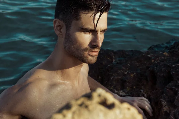 Strong face male model on the nature background with rocks sand and water on the beach on the sunset