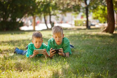 Kardeş çocuk mobil birlikte çimlere park güneşli bir günde yalan üzerinde oyun oynama