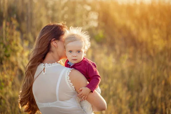 夏の畑で晴れた日を楽しむ彼女のかわいい子供を持つ若い母親 背面図 — ストック写真
