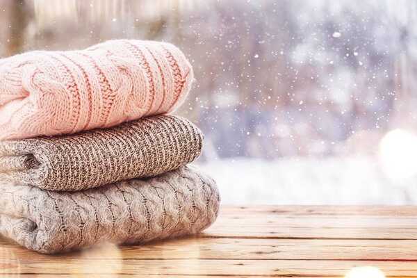 Stack of knitted sweaters on wooden tableon winter nature background.