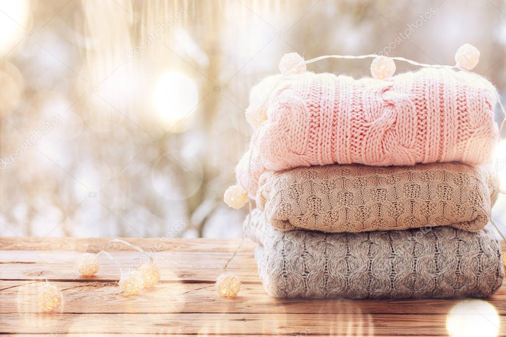 Cozy pile of knitted sweaters on wooden table on winter nature background with snow.