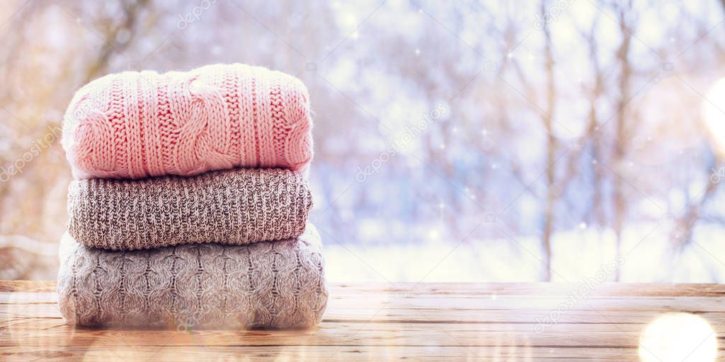 Banner. Stack of knitted sweaters on wooden table on winter nature background