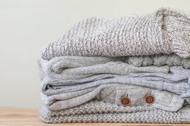 Ahşap masa üzerinde soğuk sonbahar için rahat gri kazak yığını