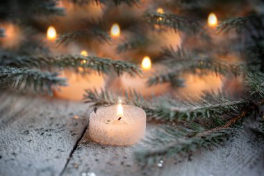 Beyaz ahşap zemin üzerinde Çamın dalları ile kar üzerinde yanan mum ve Noel dekorasyon