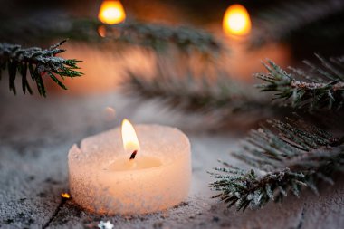 Beyaz ahşap zemin üzerinde Çamın dalları ile kar üzerinde yanan mum ve Noel dekorasyon