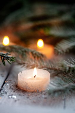 Beyaz ahşap zemin üzerinde Çamın dalları ile kar üzerinde yanan mum ve Noel dekorasyon