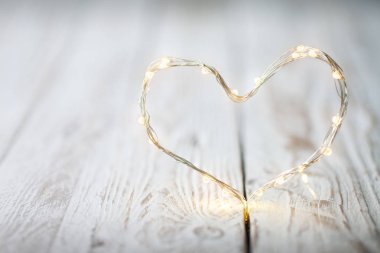 Beyaz ahşap bir masa üzerinde bir kalp şeklinde Garland ışıklar. Sevgi ve Sevgililer günü kavramı