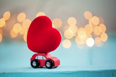 Parlatıcı bokeh arka plan üzerinde kırmızı bir kalp taşıyan minyatür kırmızı araba