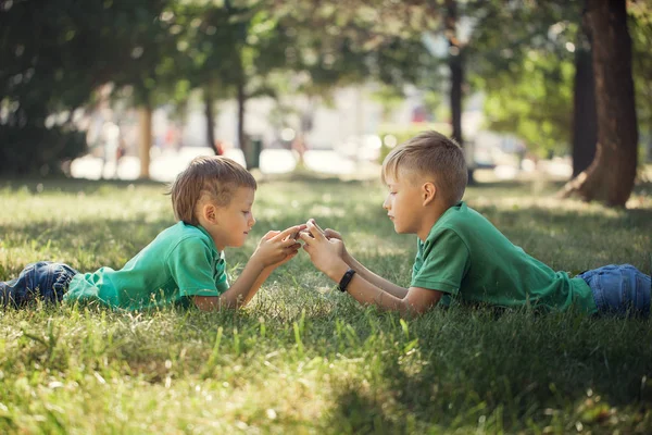 緑の草の上に横たわると 携帯電話で遊ぶ 人の子供の肖像画 — ストック写真