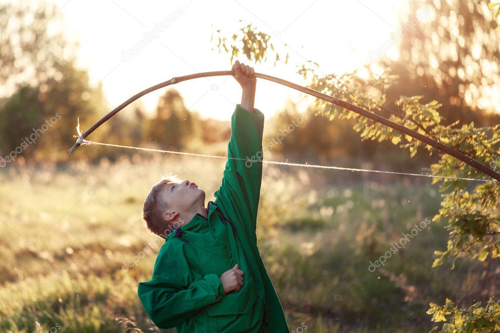 Young boy, shoot with handmade bow and arrow at target on sunset, summertime outdoor.