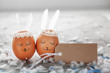 Paskalya yumurtaları ve sevimli tavşan'ın kulakları beyaz tüylü gri masada boş etiket ile dekore edilmiş.