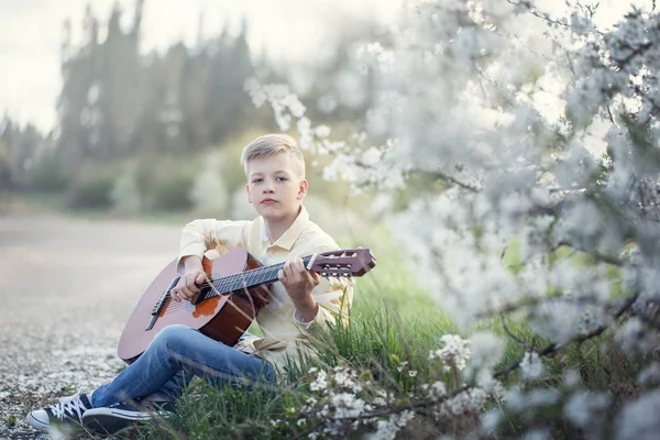 Gutaussehender Teenager mit Gitarre sitzt auf Gras im Park. — Stockfoto
