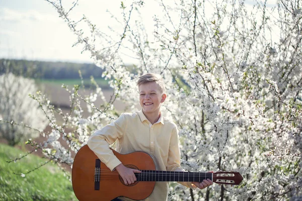 Porträt eines 11-jährigen Jungen, der im Frühlingspark steht und Gitarre spielt. — Stockfoto