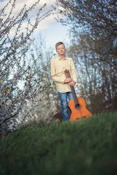 Porträt eines jungen Teenagers, der im Frühlingspark steht und Gitarre spielt. — Stockfoto