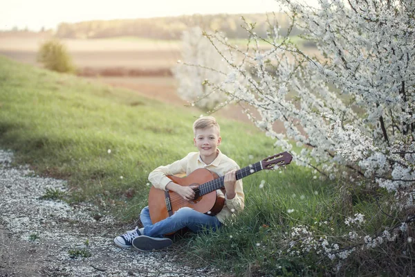 Retrato exterior de un joven adolescente tocando la guitarra en el parque de primavera . —  Fotos de Stock