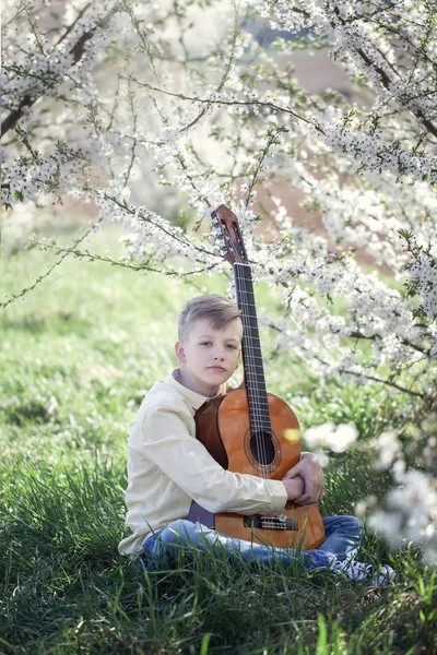 Gutaussehender Teenager mit Gitarre sitzt auf Gras im Park. — Stockfoto