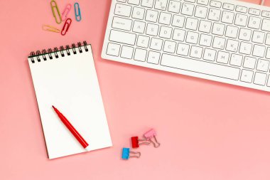 Workspace with Blank spiral notebook with keyboard on Coral Background. Top view clipart