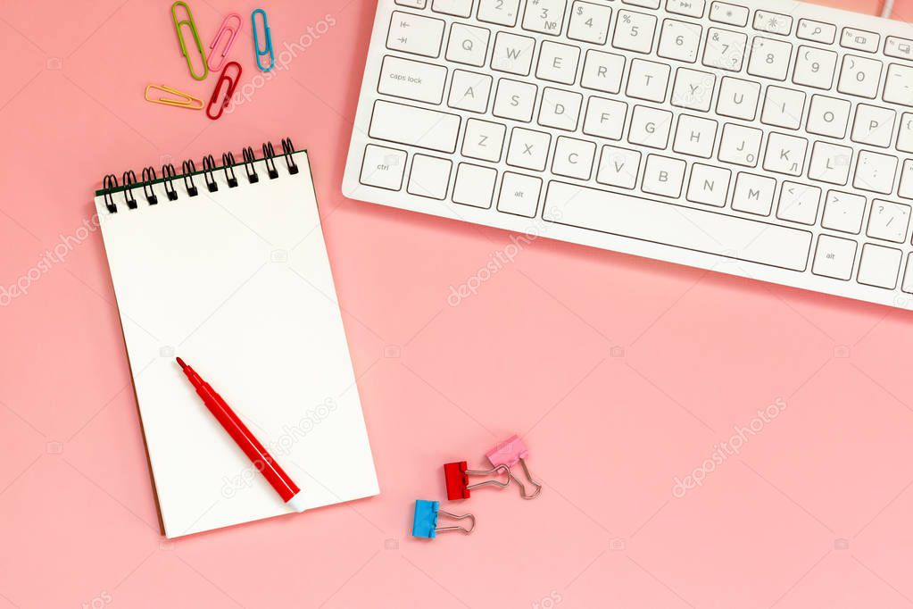 Workspace with Blank spiral notebook with keyboard on Coral Background. Top view
