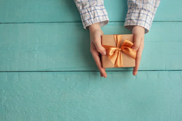 Kid's handen met luxe-geschenketui verpakt in Kraft papier en gebonden met strik. — Stockfoto