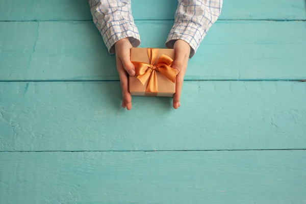 Руки мальчика держат подарочную коробку, завернутую в бумагу и завязанную бантом . — стоковое фото