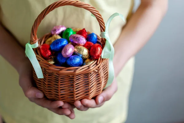 Crianças mãos segurando cesta cheia de ovos de Páscoa de chocolate . — Fotografia de Stock