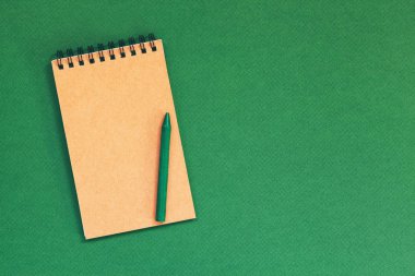 Boş spiral defter ve kalem yeşil zemin üzerine. Üstten Görünüm.