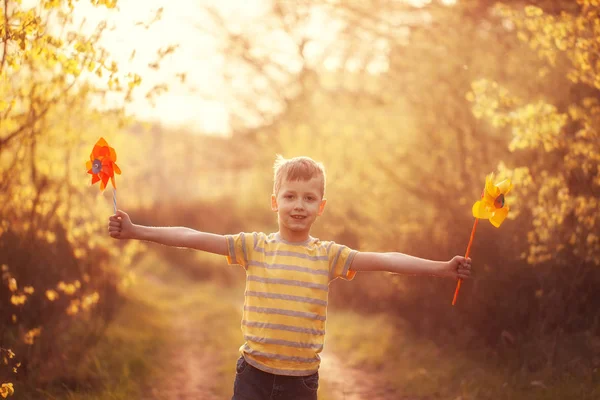 Menino correndo e segurando moinho de vento nas mãos no verão pôr do sol . — Fotografia de Stock
